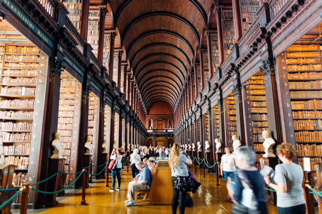 people-inside-building-2881370 Visitors explore a grand library hallway with towering bookshelves in an iconic university.